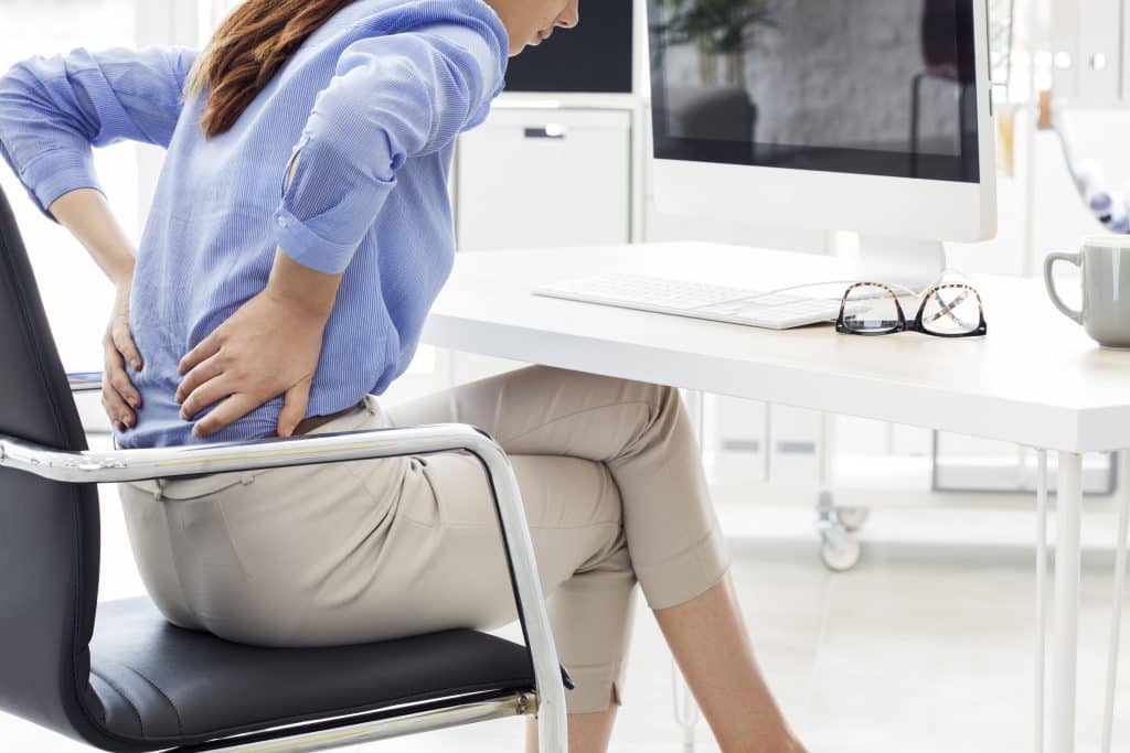 Person holding their back at an office desk