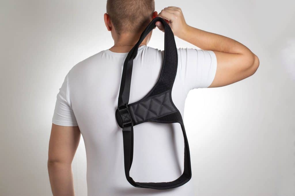 A man in a white T-shirt with a black posture corrector on a white background. How posture correctors can help back pain